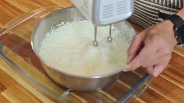 Bir kasede krema çırpmak için elektrikli mikser kullanan eller..