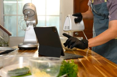 Ev aşçısı, tereyağı için krema çırparken dijital tablette tarifi takip ediyor..