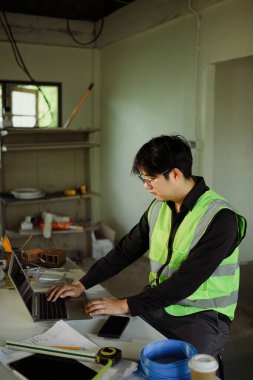 Planları gözden geçirmek ve konut yenileme çalışmalarını yönetmek için dizüstü bilgisayar kullanan mühendis.