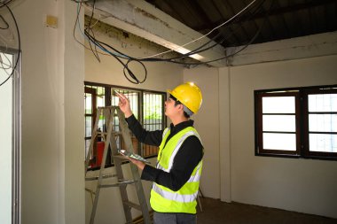 Tadilat alanında elektrik kablolarını inceleyen erkek inşaat denetçisi.