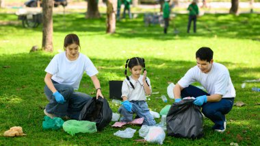 Park temizliği sırasında ebeveynler ve çocuklar birlikte plastik atık topluyorlar..