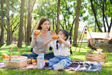Anne ve çocuk güneşli bir ormanlık alanda kamp yaparken lezzetli bir yemek yiyorlar..