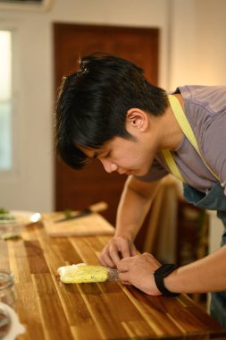 Yeni yapılmış tereyağını ahşap tezgahta plastik ambalaja saran adam..