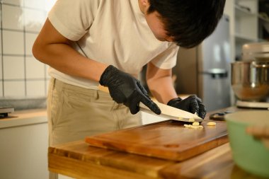 Modern bir mutfakta akşam yemeği için sarımsak doğrayan siyah eldivenli bir adam..