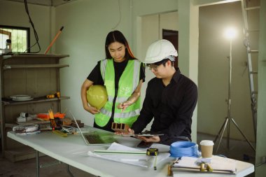 Kadın ve erkek mühendis inşaat alanında dijital tablet kullanarak proje detaylarını inceliyor.