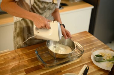 Paslanmaz çelik bir kasede krema çırpmak için el bilgisayarı kullanan adama yaklaş..