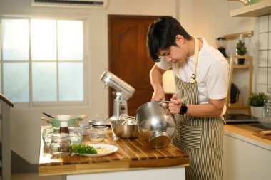 Mutfakta krem şanti hazırlayan önlük giymiş gülümseyen Asyalı adam..