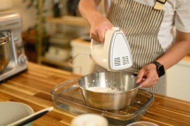 Paslanmaz çelik bir kasede krema çırpmak için el bilgisayarı kullanan adama yaklaş..