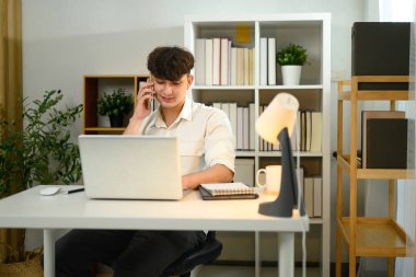 Sıraya dizüstü bilgisayarla otururken akıllı telefon konuşması yapan gülümseyen girişimci.