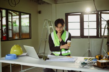 İnşaat planlarını inceleyen mühendis bir iş yerinde dizüstü bilgisayarda.