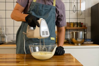 Genç Asyalı bir adam cam kasede krema yapmak için el mikseri kullanıyor..