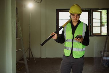 İnşaat işçisi balyoz tutuyor ve inşaat alanında akıllı telefon kullanıyor..