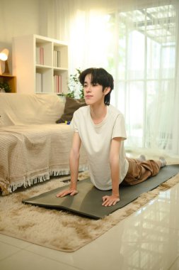 Genç adam evde yoga yaparken kobra pozu veriyor..