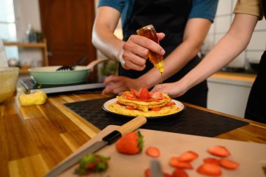 Taze çilekle kaplı ev yapımı krep yığınının üzerine şurup serpiştiren bir adam..