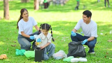 Ebeveynler ve çocuklar birlikte gönüllü olarak çöp topluyor ve bir parkı temizliyorlar..