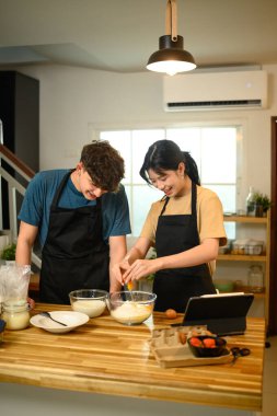 Mutfakta krep hamuru hazırlarken gülümseyen çift yumurta kırıyor..