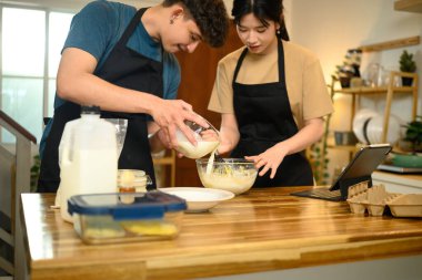 Adam mutfakta krep hamuru hazırlarken kaseye süt koyuyor..