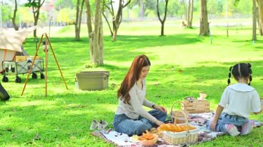 Anne ve kızı güneşli bir parkta taze ekmek ve meyvelerle battaniyede pikniğin tadını çıkarıyorlar..