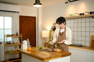 Önlüklü genç adam modern bir mutfakta basit bir kahvaltı hazırlıyor..