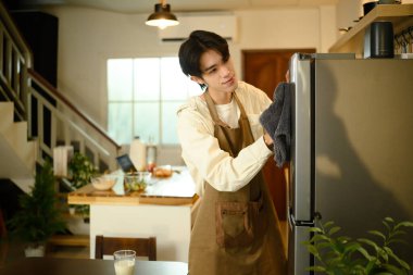 Gülümseyen adam ev işlerini yapıyor, buzdolabını bezle temizliyor..