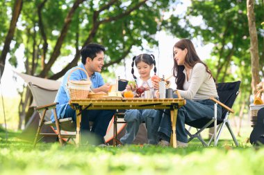 Orman parkında kamp yaparken mutlu bir aile kahvaltı yapıyor..