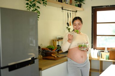 Mutlu hamile kadın taze salata yiyor, hamilelik boyunca sağlıklı beslenme alışkanlıklarını teşvik ediyor..