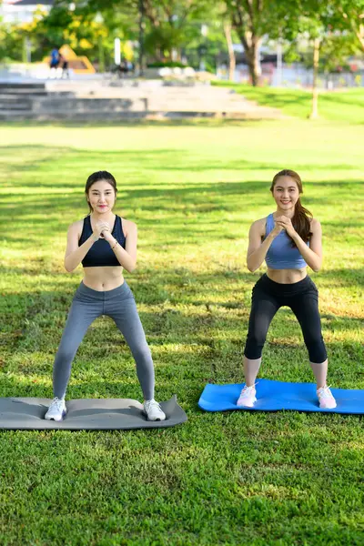 Aktif kadınlar güneşli bir parkta yoga minderlerinde birlikte çömeliyorlar..