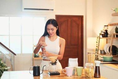 Genç bir kadın kahve çekirdeklerini öğütüyor ve sıcak bir mutfakta kahve hazırlıyor..