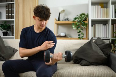 Koltukta dambıl kaldıran genç bir adam. Ev konseptinde fitness.