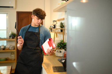 Önlüklü genç adam sıcak bir mutfakta krep karışımı talimatları okuyor..