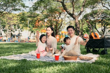 Mutlu bir aile parkta piknik yapıyor ve baloncuklarla oynuyor..
