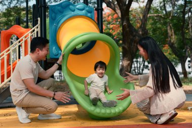 Mutlu ebeveynler parktaki renkli bir oyun parkında bebekleriyle oynuyorlar..