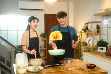 Neşeli çift, sıcak bir mutfakta kahvaltı hazırlıyor. Gülümseyerek krep çeviriyor ve gülüyor..