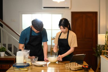 Önlüklü mutlu çift evde krep yaparken yemek tarifine uyuyorlar..