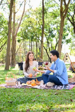 Güneşli bir ormanda kamp yaparken çiftler meyve ve kahkaha paylaşıyor..