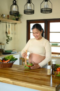 Hamile kadın mutfakta taze sebze salatası hazırlıyor..
