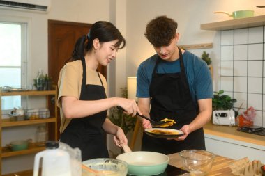 Neşeli genç çift sıcak ev mutfağında kahvaltı krepleri hazırlıyor..