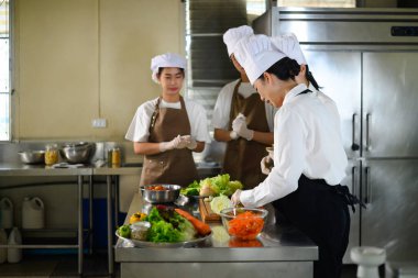 Yemek pişiren öğrenciler öğretmenlerinin yemek hazırlama tekniklerini dikkatle izliyorlar..