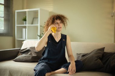 Kıvırcık saçlı kadın oturma odasında cep telefonuyla konuşuyor..