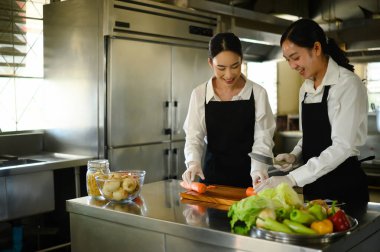 Profesyonel bir mutfakta aşçılık kursunda sebze hazırlayan iki kız öğrenci..