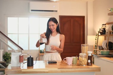 Gülümseyen kadın yeni demlenmiş kahveyi ev mutfağında fincana dolduruyor..