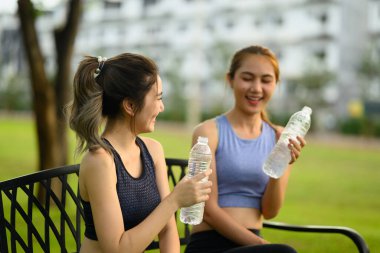 İki neşeli bayan arkadaş antrenmandan sonra şişelenmiş suyla serinliyorlar..