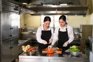 Aşçılık hocası bir öğrenciye pratik bir yemek kursunda havuç dilimleme konusunda rehberlik ediyor..