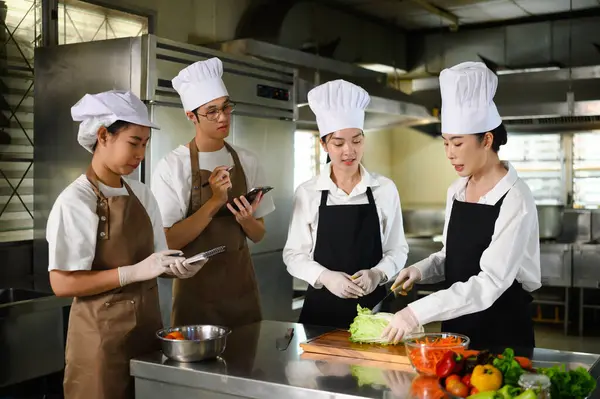 Yemek pişiren öğrenciler öğretmenlerinin yemek hazırlama tekniklerini dikkatle izliyorlar..