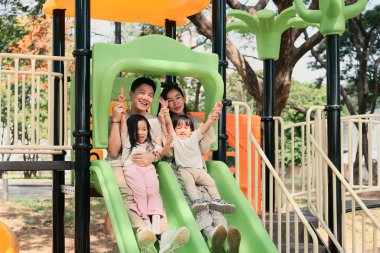 Dört kişilik mutlu bir aile oyun alanında birlikte kayıyor..