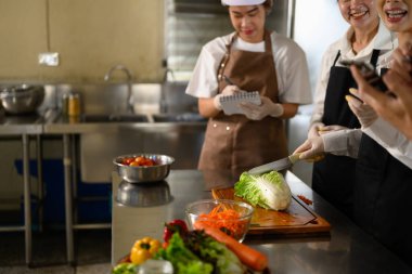 Yemek pişiren öğrenciler öğretmenlerinin yemek hazırlama tekniklerini dikkatle izliyorlar..
