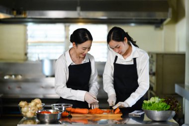 Aşçılık hocası bir öğrenciye pratik bir yemek kursunda havuç dilimleme konusunda rehberlik ediyor..