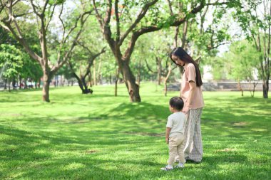 Güneşli bir günde huzur dolu yeşil bir parkta el ele tutuşan anne ve bebek..