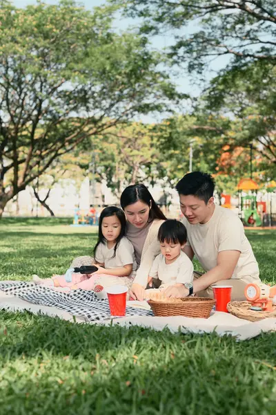 Ebeveynler ve iki çocuk yeşil bir parkta hafta sonu pikniği sırasında keyifli bir açık hava yemeğini paylaşıyorlar..