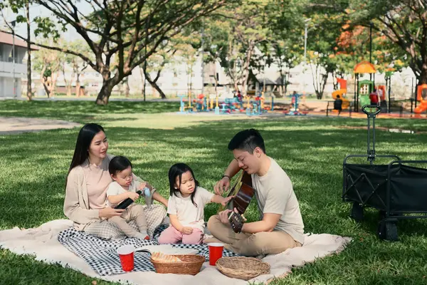 Ebeveynler ve iki çocuk yeşil bir parkta hafta sonu pikniği sırasında keyifli bir açık hava yemeğini paylaşıyorlar..